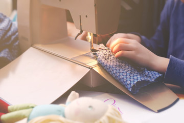 Enthusiastic young girl sews a toy dress for her doll at a compact sewing machine under supervision of her mother - background and foreground blanked out blurry