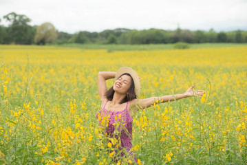 asia woman with a hat in her hand walks in a field with field flowers and smiles sincerely, happy...