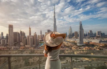 Fotobehang Dubai Vrouw met een witte hoed staat op een balkon voor de skyline van Dubai Downtown