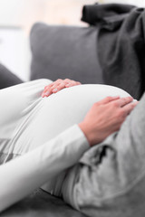 Fototapeta premium Pregnant tired exhausted woman with stomach issues at home on a couch, being sick.