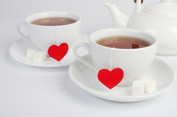 Two white cups of tea with tea labels in the form of red hearts. Light background.