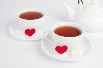Two white cups of tea with tea labels in the form of red hearts. Light background.