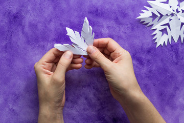 Woman hands unfolding paper to reveal snowflake on the violet surface