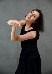 Model Standing right in front of the camera with vivid emotions. Vertical portrait of a cute smiling brunette woman in black dress on gray alternative background.