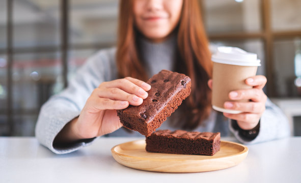 Closeup image of a beautiful woman holding and eating a piece of brownie cake while drinking coffee
