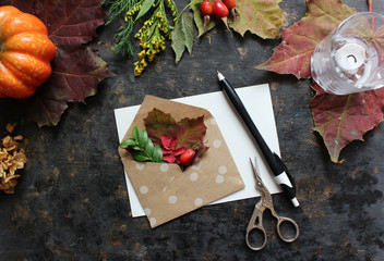 Autumn background: fallen leaves, dry petals, dried flowers and plants on white with envelope full of autumn leaves . Top view. Flat lay.