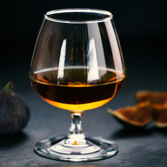 Whiskey or cognac in a glass and figs on dark concrete