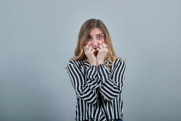 Scared young blonde woman in fashion black and white striped shirt looking at camera, biting nails...