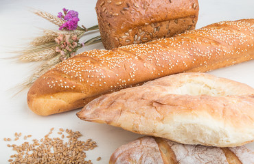 Different kinds of fresh baked bread on a white wooden background. side view.