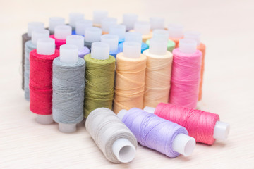 threads on spools of different colors on a light wooden table. Three spools of thread are lying. Sewing and atelier hobby concept.