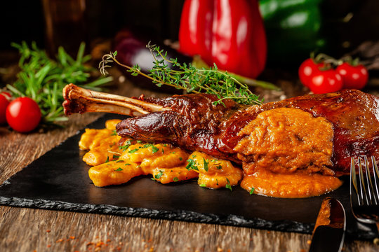 Serbian, Balkan cuisine. Lamb of leg with gnocchi. Serving in a restaurant on a black slate, on wooden table. background image, copy space