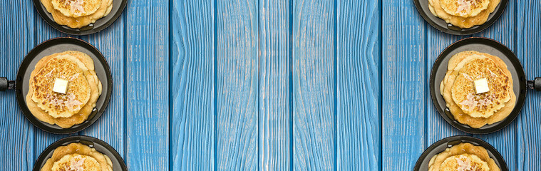 Hot delicious pancakes in frying pans on blue wooden table. Pancake week. Panoramic banner.