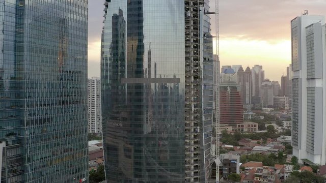Reveal Aerial view of Jakarta skyline near casablanca flyover with trees in foreground showing City Skyscrapers before sunset. motorbikes passing. Dolly Motion of construction building