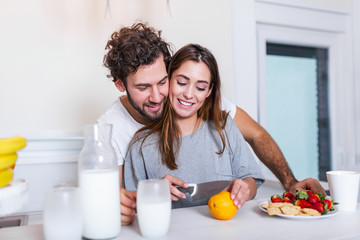 Beautiful young sports couple are talking and smiling while cooking healthy food in kitchen at home. Lovely couple in the kitchen making orange juice