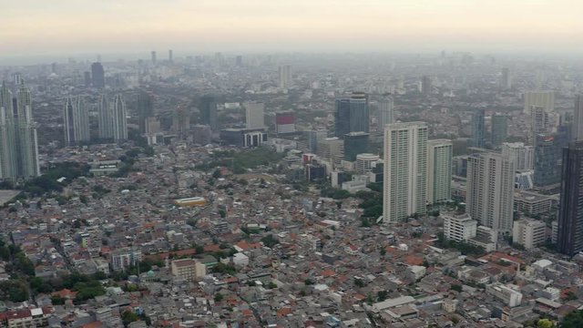 Aerial view of skyscrapers in Jakarta with building in construction before beautiful sunset and cloudy sky.  Fast Dolly motion