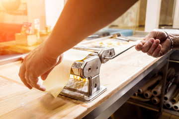 Chef rolling dough with a pasta machine. Pasta maker machine. Homemade italian style cuisine. Restaurant.