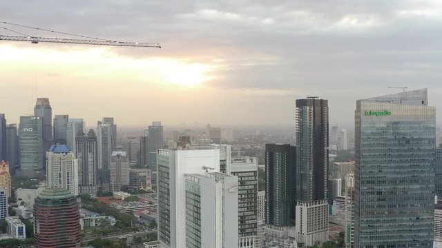 Aerial view of skyscrapers in Jakarta with building in construction before beautiful sunset. Construction with Cranes. Dolly motion