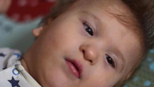 Portrait of a baby with cerebral palsy lying on his back and playing at home. Special needs child. Handicapped baby boy close-up.