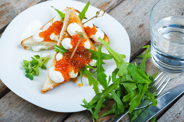 Classic breakfast, hot sandwich with red salmon caviar and mozzarella on a plate on a wooden table. Hand-made, rustic breakfast, toast with caviar, cheese and greens. Soft focus.