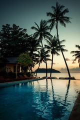 Beautiful poolside and sunset sky. Luxurious tropical beach landscape, deck chairs and loungers and water reflection.
