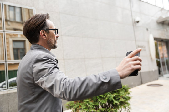 Image of mature businessman holding cellphone and pointing finger