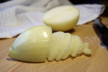 sliced onion in half rings close up on a wooden cutting Board in the background a white towel and half an onion on the left a knife with a wooden handle