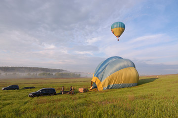 Obraz premium Hot-air balloon drifting in the sky, car and trailer with equipment set on the ground