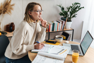 Photo of woman making notes in exercise book and using laptop