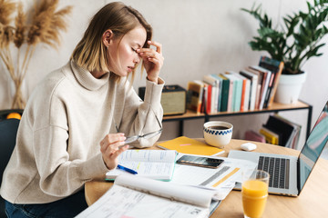 Photo of tired woman making notes in exercise book and using laptop