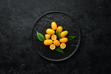 Kumquat on a black stone background. Citrus fruits. Top view. Free space for your text.