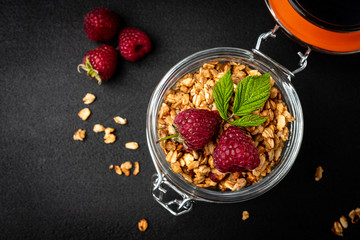 Granola in glass jar and raspberry on black background.