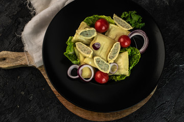 traditional German maultaschen with the addition of purple onion, fresh tomatoes and young salad on a dark background