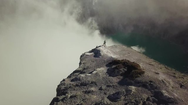 Epic Cinematic Aerial Shot of Man Standing on Edge of Crater Rim on a Volcano Pan Down to Cliff into Smoke