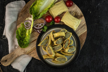 traditional German maultaschen with the addition of purple onion, fresh tomatoes and young salad on a dark background