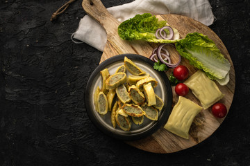 traditional German maultaschen with the addition of purple onion, fresh tomatoes and young salad on a dark background