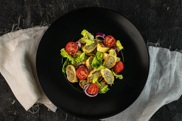 traditional German maultaschen, baked with purple onion, fresh tomatoes and young salad on a dark background