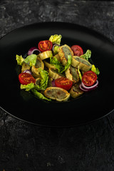 traditional German maultaschen, baked with purple onion, fresh tomatoes and young salad on a dark background