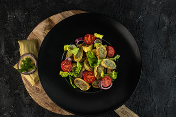 traditional German maultaschen, baked with purple onion, fresh tomatoes and young salad on a dark background