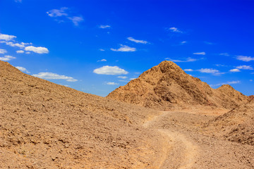 picturesque dry desert landscape dirt trail and sand stone rocks and hills of Eilat mountains in the most south region of Israel summer time clear weather day, vivid blur sky background, copy space