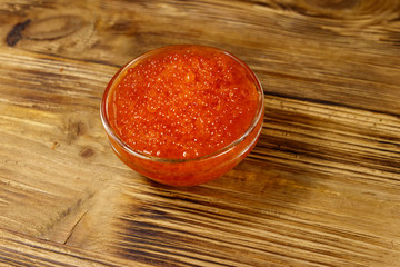 Red caviar in glass bowl on wooden table