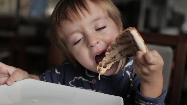 Close up of little cute boy eating pizza. Neutral colors for collor correction.