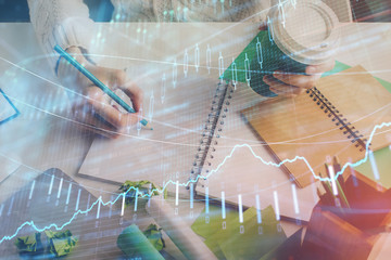 Financial forex graph displayed on hands taking notes background. Concept of research. Multi...