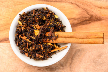 Chai Spices and a Cinnamon stick in a white bowl and a wooden table in a white