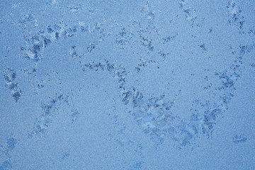Ice and frost on a window pane in winter. Weather forecast: cold, frost, cooling. Abstract background or wallpaper in bright blue. Reduced weakened contrast. Harsh season