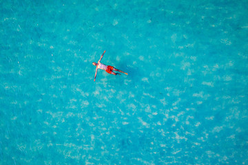 Drone view of a man floating in tropical sea water. Aerial view of young man floating on sea water enjoying sunbathing and vacations in tropical destination. People travel tourism holidays concept.