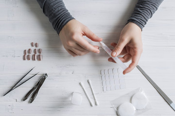 The process of putting artificial (fake) fingernail on the finger. Woman manicure. Flat lay.