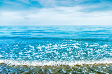Blue sea water with waves, foam and white clouds on the sky. Calm tropical landscape