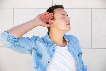 Joyful student guy with closed eyes making listening sign with hand at ear. Portrait of handsome...