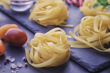 Pasta on the table with spices and vegetables. Noodles with vegetables for cooking on a black stone background.