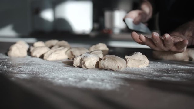 Low Angle View Of Fresh Dough Being Sliced Into Smaller Pieces On Kitchen Table. Slow Motion